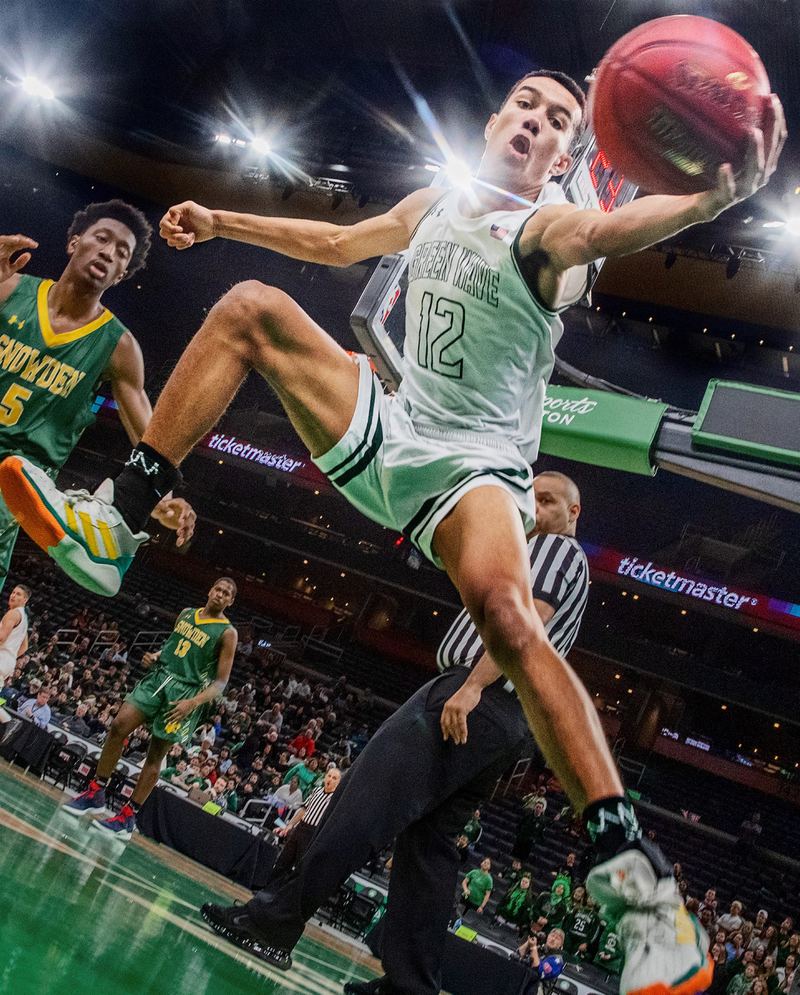 A basketball player in a white number 12 jersey flies sideways through the air to grab a loose ball in a packed arena