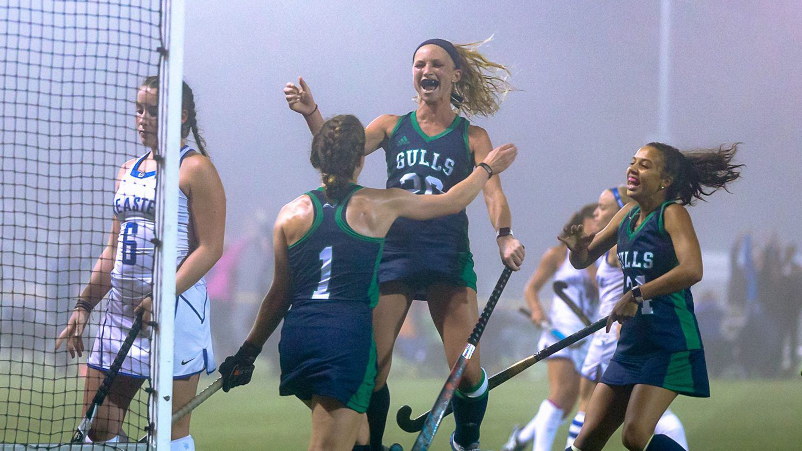 Field hockey players run in to celebrate a goal on a foggy night