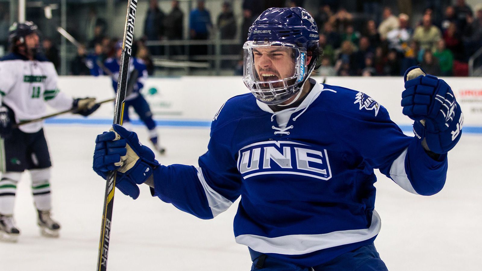 A hockey player in a blue jersey shouts and celebrates a goal